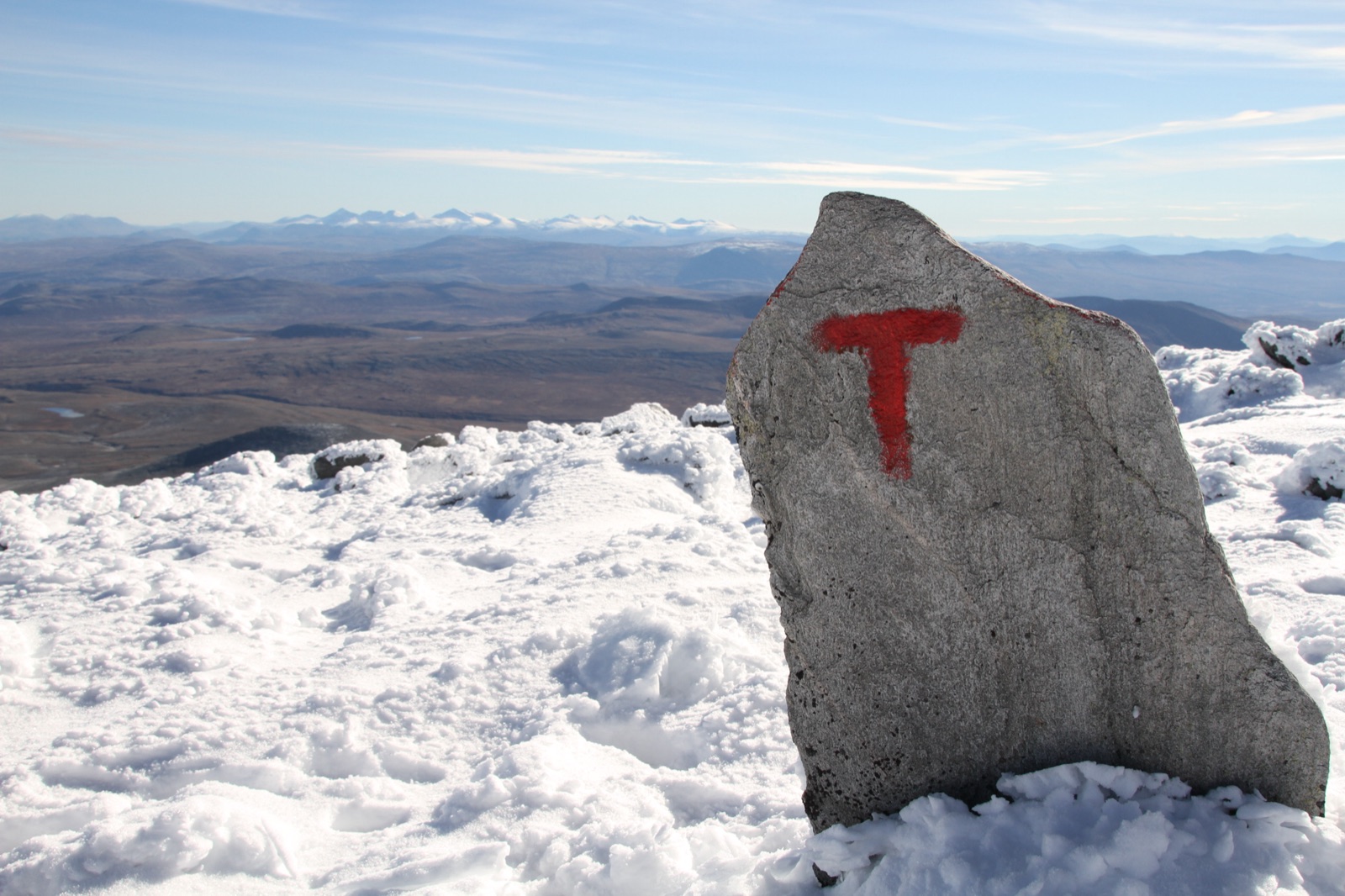 DNT-merket T-stein på snødekt fjelltopp.