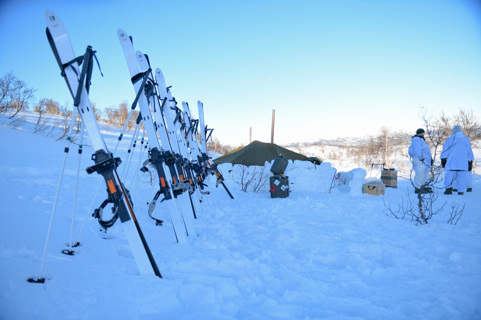 Winter camp — skis stood up beside a tent with a stove pipe in a snowy landscape