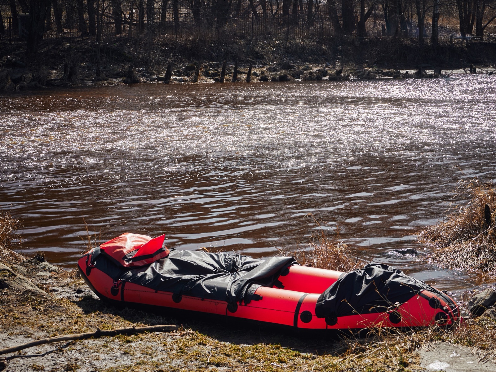 Packraft på speilblank fjellsjø, med ryggsekk og åre i forkant